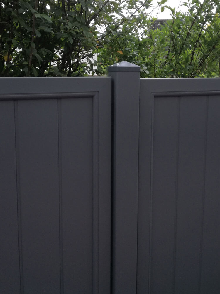 Anthrazitgraue Sichtschutzelemente an mittigen Pfosten mit Spitzkappe befestigt, dahinter Bäume und Sträucher