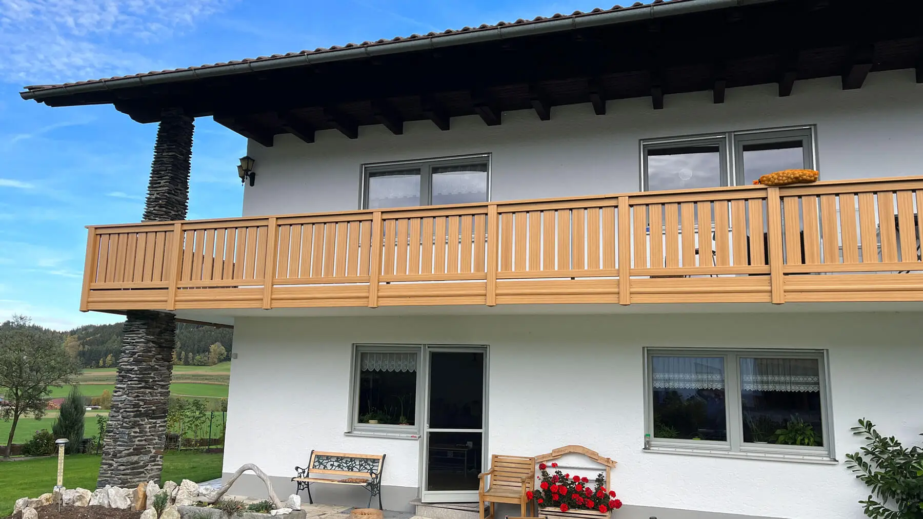 Kunststoff-Balkon Modell Gräfelfing in Lärche-Dekor an weißem Haus, ohne Blumenkasten, mit Garten und Steinmauer