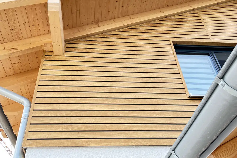 Kunststoff-Fassadenverkleidung Desert Oak mit schwarzer Schattennut an Hausfassade unter Dachvorsprung mit sichtbaren Holzbalken
