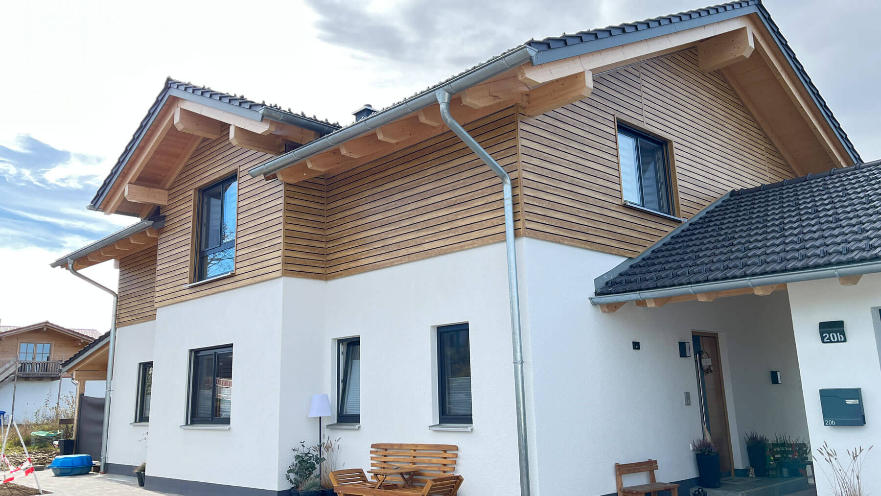 Modernes Haus mit Kunststoff-Fassadenverkleidung Desert Oak und schwarzer Schatten-Nut im oberen Bereich, weiß verputzter unterer Bereich, sichtbare Dachkonstruktion und Fenster