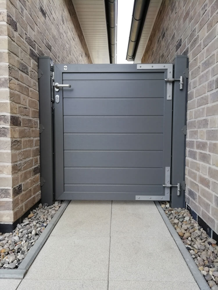 Sichtschutz-Einzeltor Serie 21H in basaltgrau, glatt, zwischen zwei Backsteinwänden mit Metallbeschlägen und Schloss