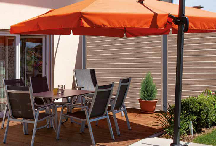 Kunststoff-Sichtschutzwände mit waagrechten Rhombusprofilen in Holzoptik auf einer Terrasse mit orangefarbenem Sonnenschirm und Sitzgruppe mit Stühlen und Tisch