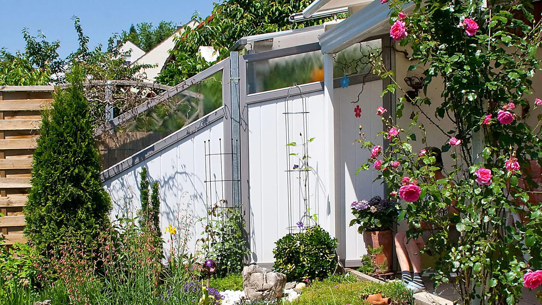 Garten mit blühenden Pflanzen und Kunststoff-Sichtschutz Serie 82 in Weiß, angrenzend an ein Haus mit Terrasse