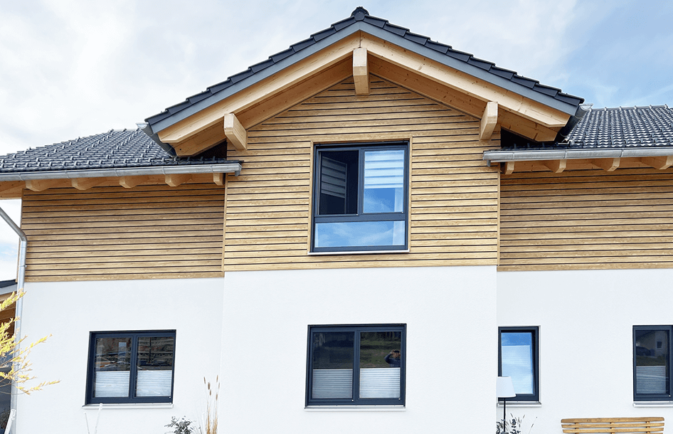 Hausfassade mit Kunststoff-Fassadenverkleidung im Dekor Desert Oak mit schwarzer Schattennut und weißen Putzflächen, drei Fenster und Satteldach mit Dachziegeln