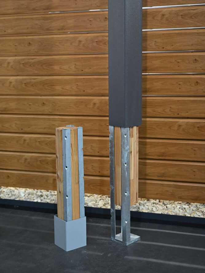 Detailansicht Pfostenanker zum Aufdübeln mit Lärchenholz-Inlay und Kunststoff-Pfostenhülle vor Kunststoff-Sichtschutzwand in Holzoptik