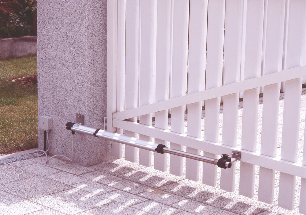 Nahaufnahme eines Torantriebes befestigt an einer Steinsäule und einem Torflügel aus weißen Kunstostoff-Zaunlatten