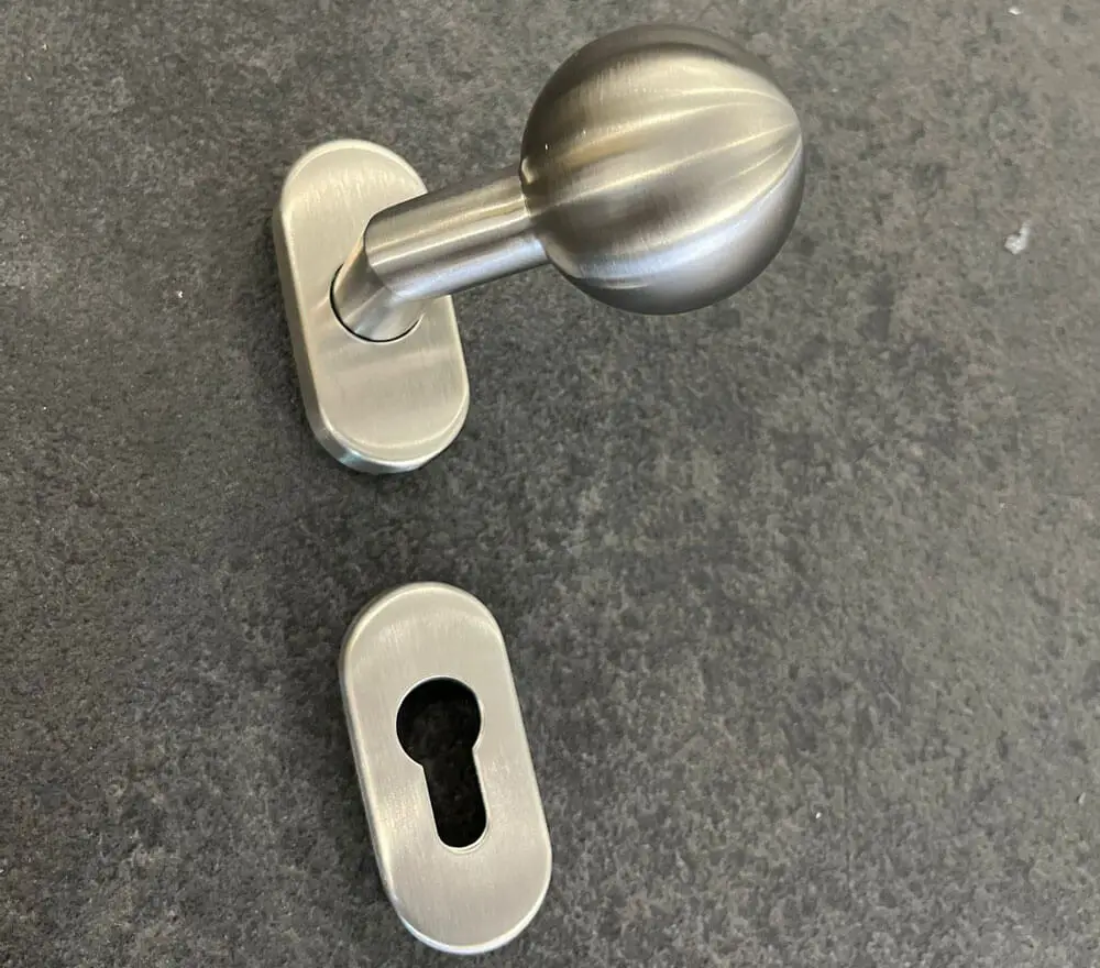 Edelstahl Türdrücker mit Knopf und Zylinder-Schutzrosette auf grauem Untergrund abgebildet
