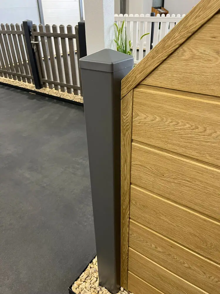 grauer Kunststoffpfosten 100x100 mm mit spitzer Abdeckung neben Sichtschutztafel in Holzoptik mit horizontalen Lamellen