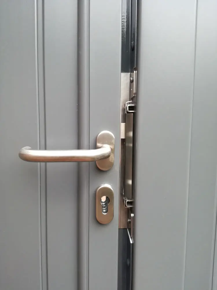 Türdrücker mit Anschlagblech an grauer Tür, Edelstahlgriff und Schlüsselloch sichtbar