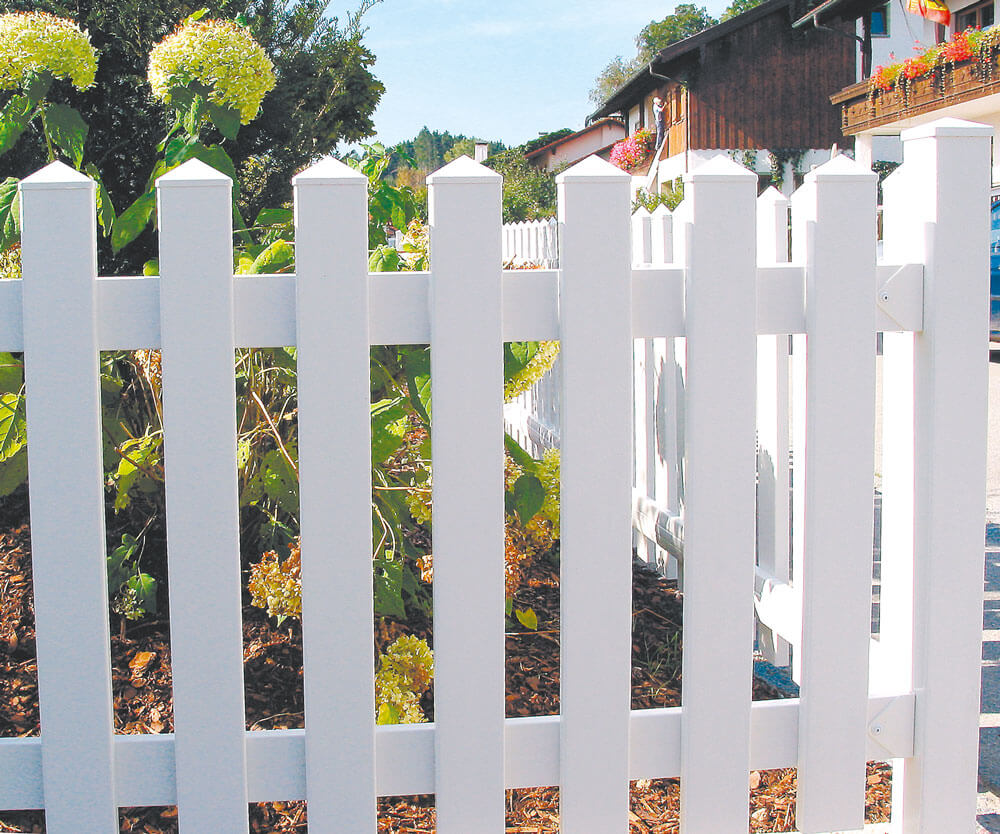 Weißes Kunststoff-Zaun-Element Modell Saaletal mit Spitzkappen vor einem Garten mit bunten Blumen